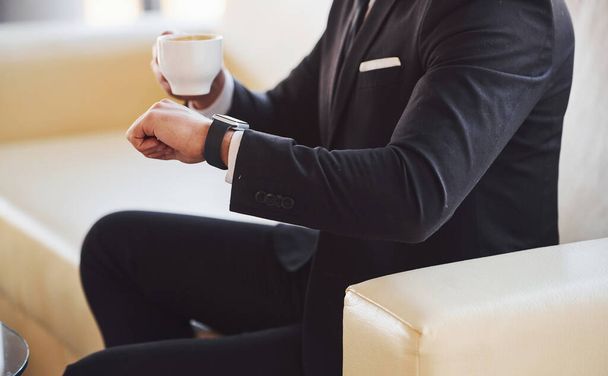 Close up view of young businessman in black suit and tie with cup f drink checking time. - Photo, image