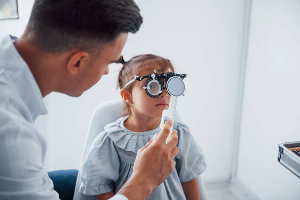 Testing vision. Young ophthalmologist is with little female visitor in the clinic. - 写真・画像