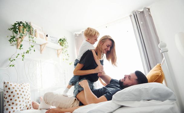 Young married couple with their young son lying down on bed and have fun together in bedroom at daytime. - Fotografie, Obrázek