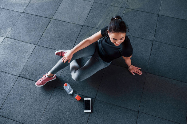 Top view of young woman in sportive clothes that sits on the floor with water in the gym. - Foto, immagini