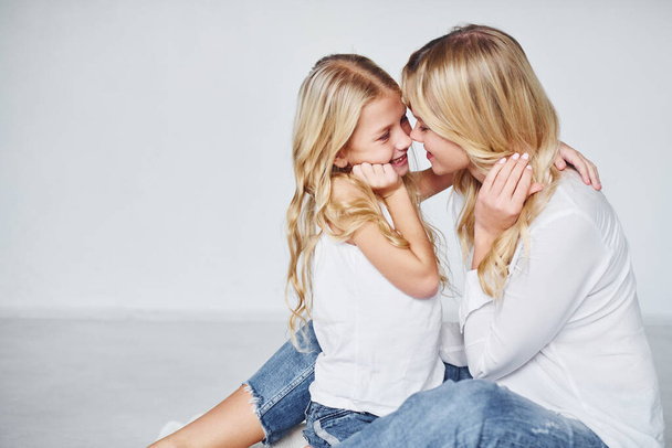 Mother with her daughter together is on the ground in the studio with white background. - Foto, imagen