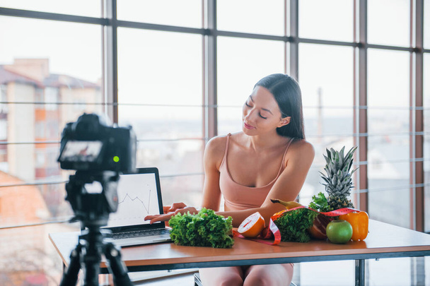 Young fitness vlogger doing video indoors by sitting near table with healthy food. - Foto, Bild