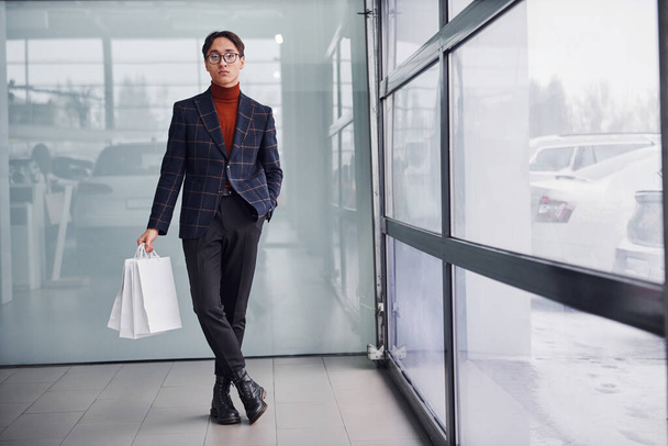 With shopping bags. Young business man in luxury suit and formal clothes is indoors in the office. - Foto, Imagem