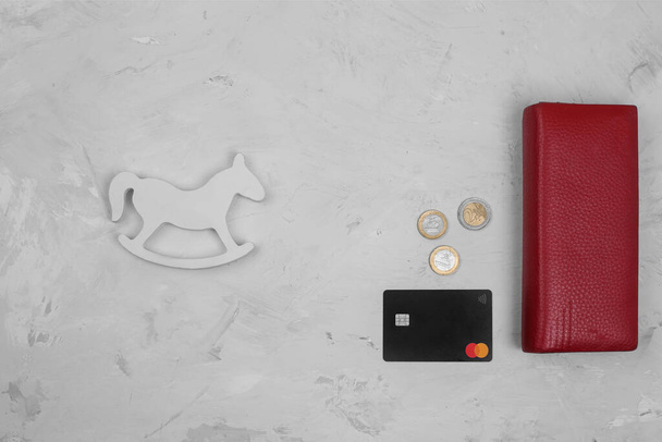 Wallet, credit card, coins and baby rattle on a gray stone background. Flat lay, copyspace. Parenting expenses concept. Working out a baby budget. Saving money when planning for a newborn. - Photo, Image