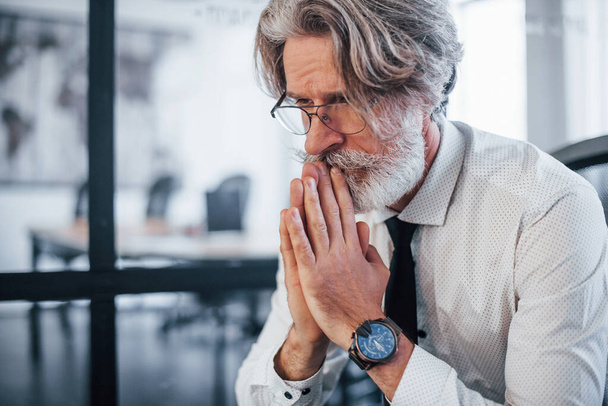 Serious mature businessman with grey hair and beard in formal clothes sitting in the office. - Fotoğraf, Görsel