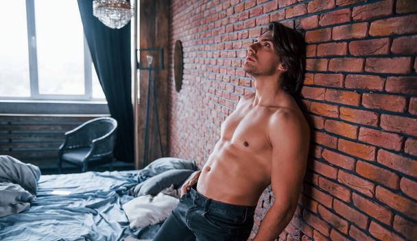 Shirtless sexy man leaning on the brick wall in bedroom at morning time. - Foto, afbeelding