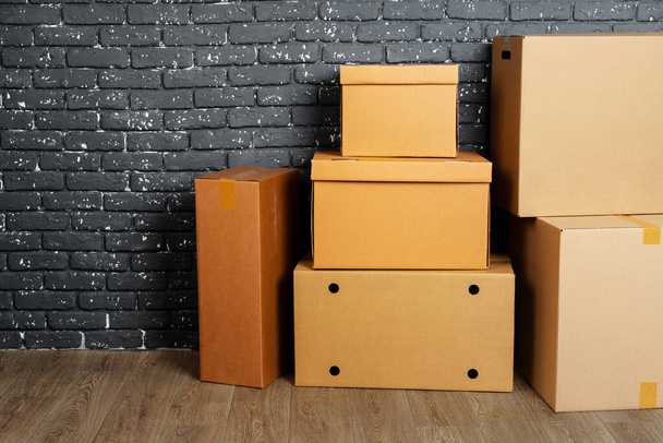 Stack of cardboard boxes in the empty room against black brick wall - Foto, imagen