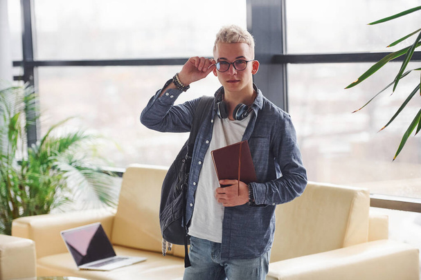 Young hipster guy in nice clothes standing indoors with notepad. - Photo, image