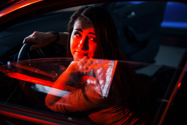 Young woman is inside of brand new modern automobile with red lighting. - Foto, Bild