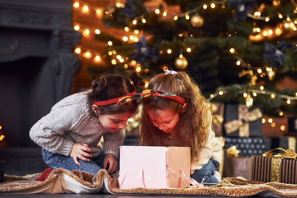 Two little girls have fun in christmas decorated room with gift boxes. - Фото, изображение