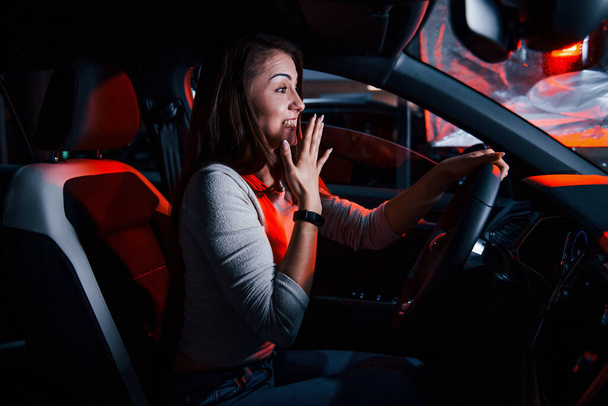 Young woman is inside of brand new modern automobile with red lighting. - Valokuva, kuva