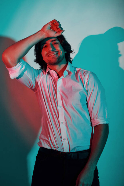 Портрет молодого стильного человека, стоящего в неоновом свете в студии. - Фото, изображение