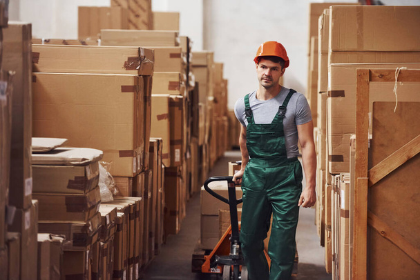 Young male worker in uniform is in the warehouse with pallet truck. - Fotografie, Obrázek