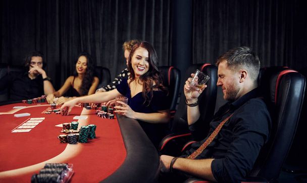 Ομάδα κομψών νέων που παίζουν πόκερ στο καζίνο μαζί. - Φωτογραφία, εικόνα