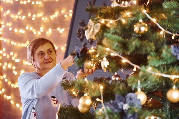 Old woman decorating christmas tree indoors in the room. - Photo, Image