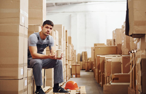 Storage worker sits and have a break. Eats sandwitch and drinks coffee. - 写真・画像