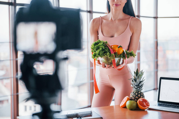 Young fitness vlogger doing video indoors by standing near table with healthy food and laptop. - Foto, Bild