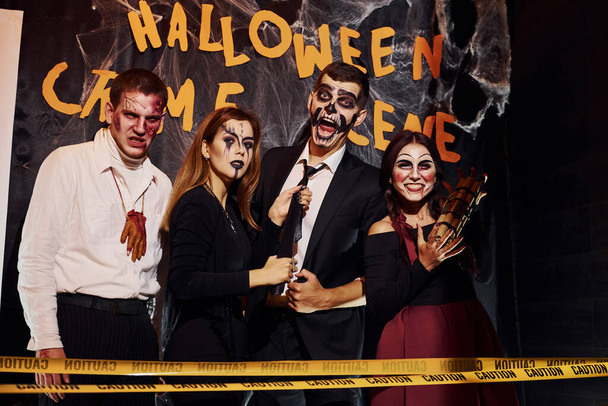 Standing against crime scene wall. Friends is on the thematic halloween party in scary makeup and costumes. - Fotó, kép