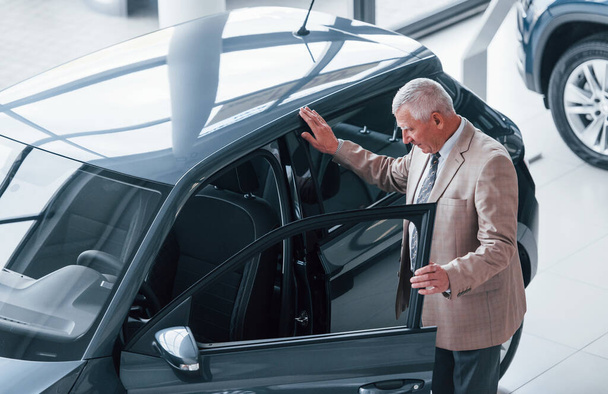 Aged man in formal wear walking in the automobile salon and looking for the car. - Foto, Bild