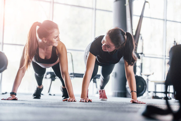 Two young girls in sportive clothes is in the gym doing exercises together. - Photo, Image