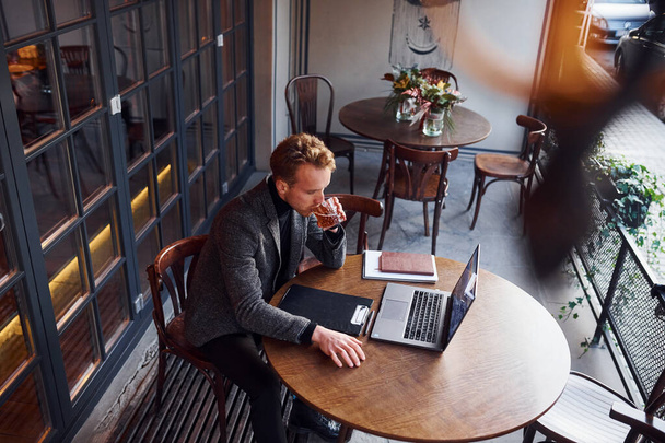Top view of elegant young guy in formal wear that sits in cafe with his laptop. - Valokuva, kuva