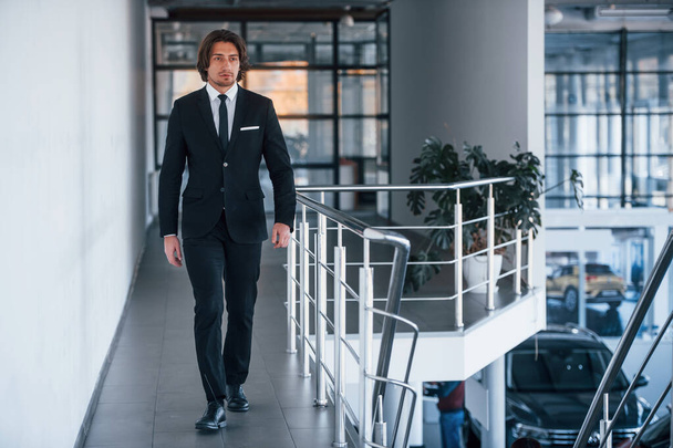 Portrait of handsome young businessman in black suit and tie walks indoors. - Fotó, kép