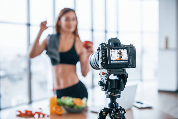 Female vlogger with sportive body standing indoors near table with healthy food. - Foto, afbeelding
