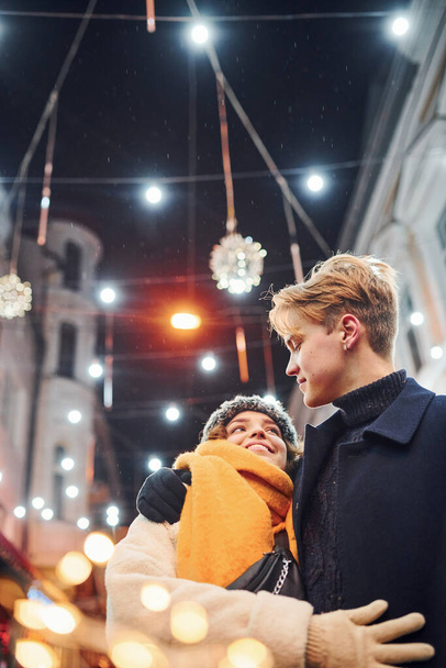 Happy young couple in warm clothes is on christmas decorated street together. - Fotoğraf, Görsel