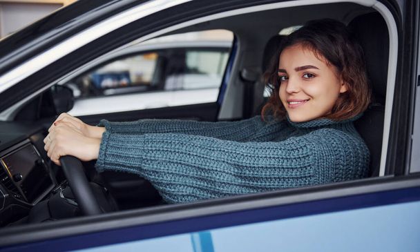 Positive young girl in casual clothes sitting inside of modern car and smiling. - Zdjęcie, obraz