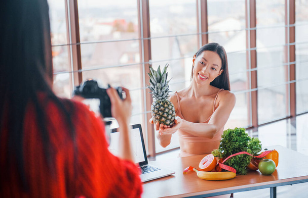 Fitness model have photoshoot by female photographer indoors by the table with healthy food. - Fotó, kép