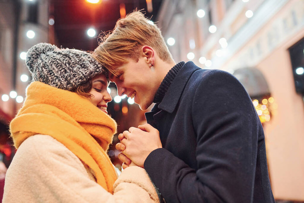 Closeness of the people. Happy young couple in warm clothes is on christmas decorated street together. - Fotoğraf, Görsel