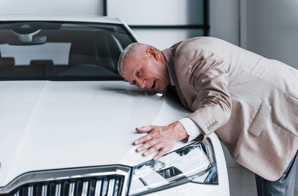 Cheerful aged man in formal wear stands in front of modern white car. - Photo, image