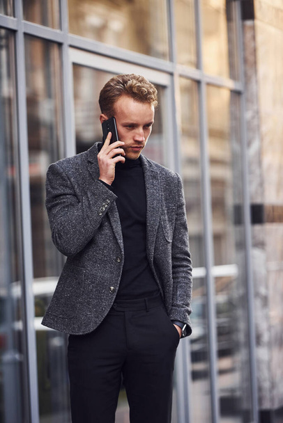 Man in elegant formal wear outside against modern building talking by the phone. - Photo, image