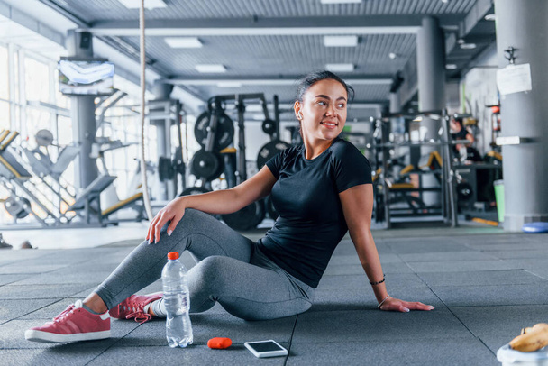 Young girl in sportive clothes taking a break with food and water is in the gym at daytime. - 写真・画像