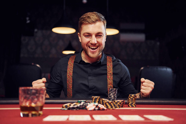 Happy elegant young man sits in casino and celebrate his victory in poker game. - 写真・画像