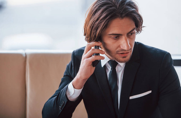 Portrait of handsome young businessman in black suit and tie sits and have a call. - Фото, изображение