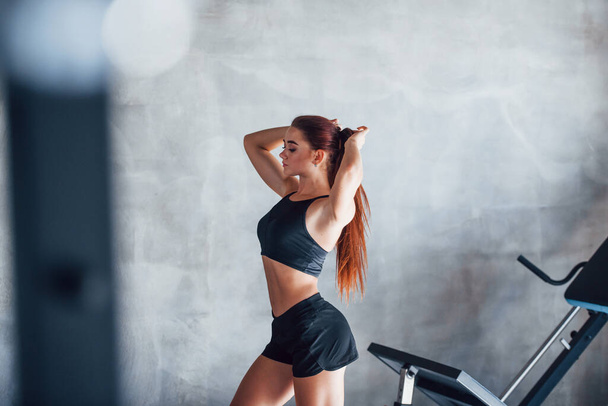 Young fitness woman with slim type of body and in black sportive clothes is in the gym. - Fotoğraf, Görsel