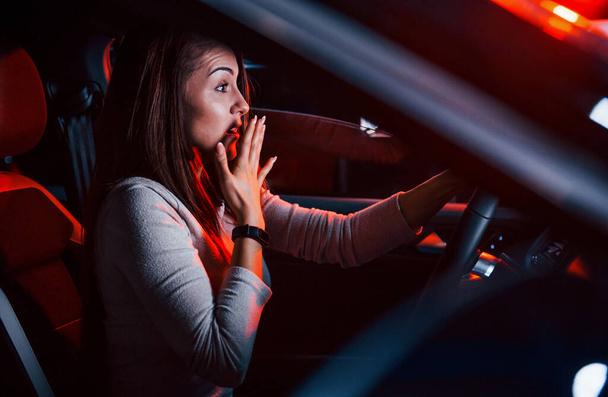 Young woman is inside of brand new modern automobile with red lighting. - Valokuva, kuva