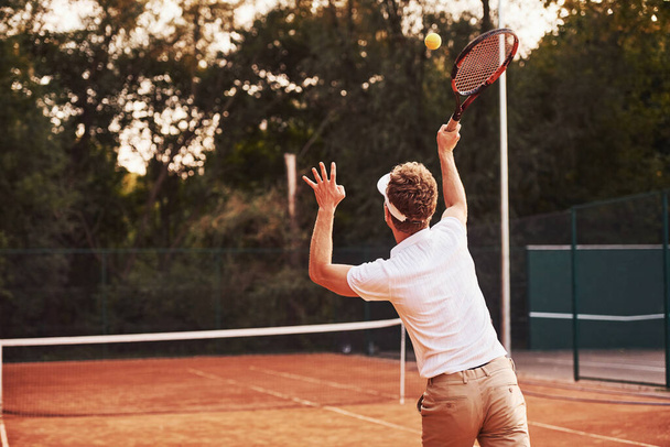 Young tennis player in sportive clothes is on the court outdoors. - Foto, afbeelding