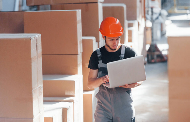 Storage worker in uniform and modern laptop in hands checks production. - Foto, immagini