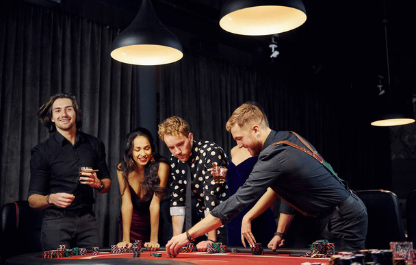 Ludzie w eleganckich ubraniach stojący i grający w pokera w kasynie razem. - Zdjęcie, obraz