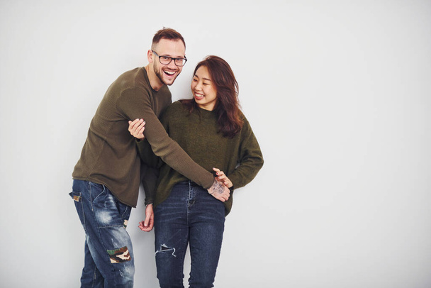 Happy multi ethnic couple in casual clothes is together indoors in the studio. Caucasian guy with asian girlfriend. - Valokuva, kuva