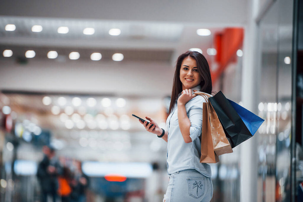 Brunette woman in the supermarket with many of packages and phone in hands have shopping day. - Foto, Imagen