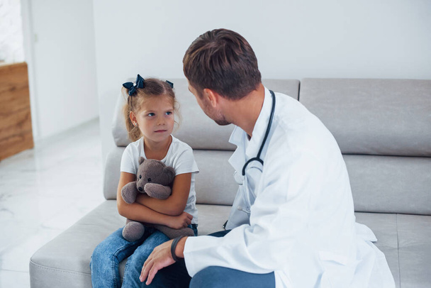 Male doctor in white uniform sits in the clinic with little girl. - Foto, imagen