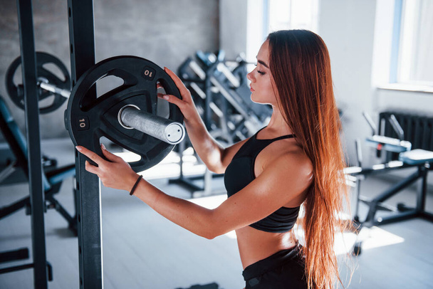 Young fitness woman with slim type of body and in black sportive clothes is in the gym. - Фото, зображення