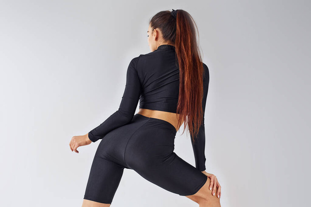 Twerk dancing. Sportive woman in black clothes in the studio against white background. - Фото, изображение