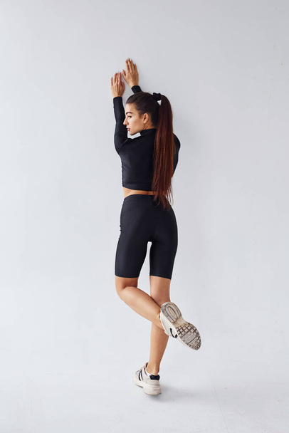 Sportive woman in black clothes doing exercises in the studio against white background. - Foto, afbeelding