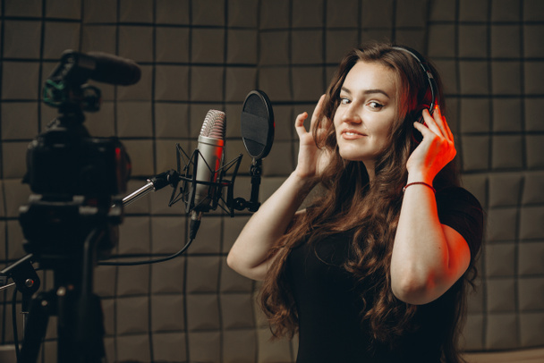 Young girl with microphone and headphones in recording studio. Recording of vocal, blogger, reading text, voice acting. - Photo, Image