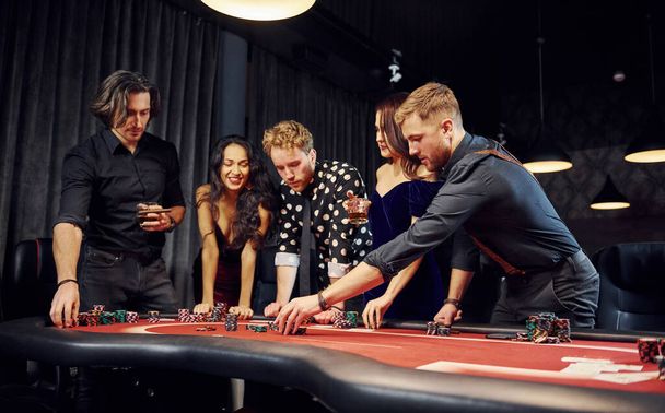 Άνθρωποι με κομψά ρούχα που στέκονται και παίζουν πόκερ στο καζίνο μαζί. - Φωτογραφία, εικόνα