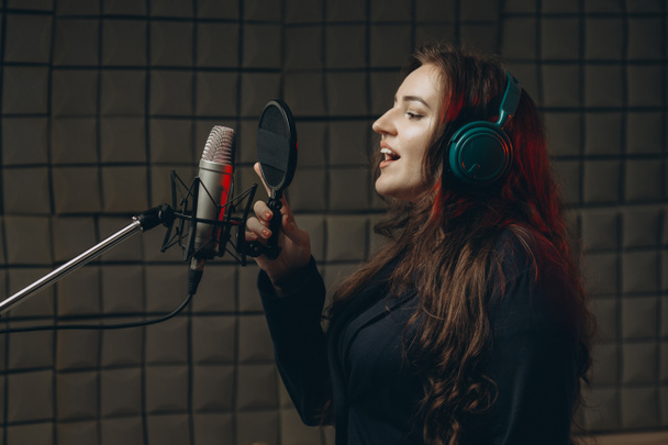 Женщина с микрофоном записывает голос для дубляжа в музыкальной студии - Фото, изображение
